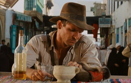 Harrison Ford sits at a table dressed as Indiana Jones