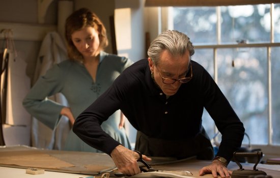 A woman watches on as a man takes some scissors to a piece of fabric.