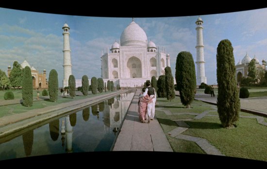 A couple walk in front of the Taj Mahal, displayed on a Cinerama curve.