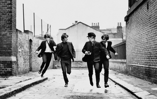 A black and white image of The Beatles running down a cobbled street