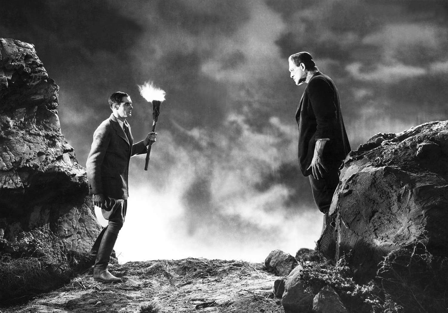 A black and white image from Frankenstein featuring the monster encountering a man with a flaming torch.