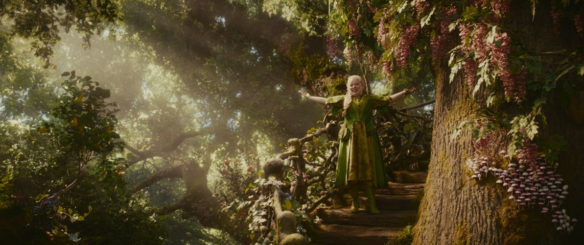 Nicola Coughlan stands in the middle of a magical forest scene with her arms out wide.