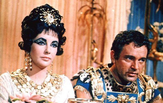 Elizabeth Taylor and Richard Burton sit side by side dressed in historical Egyptian clothing.