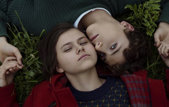 A young man and woman lay side by side with their cheeks touching.