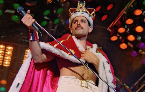 Freddie Mercury performs on stage wearing a crown and cape.