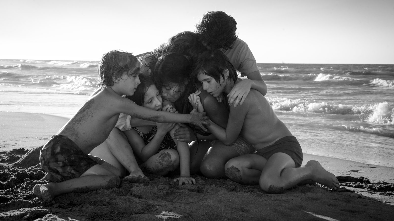 A still from Roma of a family hugging on the beach