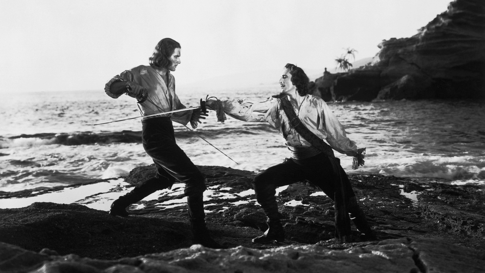 Two men swordfight by the sea.