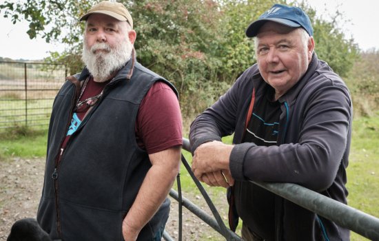 Two farmers stand either side of a fence
