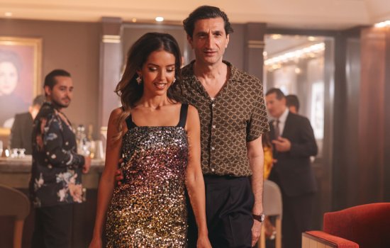 A  man and woman dressed sharply stand side by side in a bar.