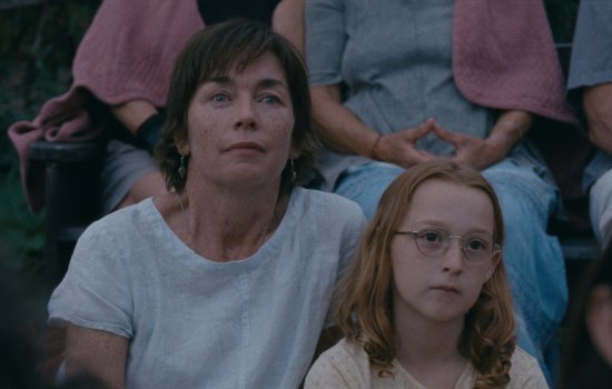 A woman and young girl sit together in a crowd, watching something off-camera.