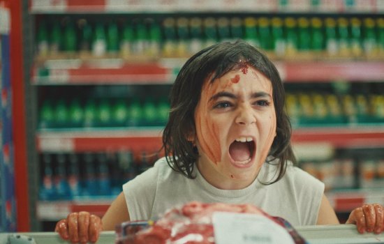 A child stands in a supermarket, covered in tomato sauce, screaming at someone behind a counter.