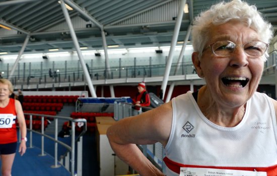 A woman stands in the middle of a sports arena smiling, wearing sporting gear.