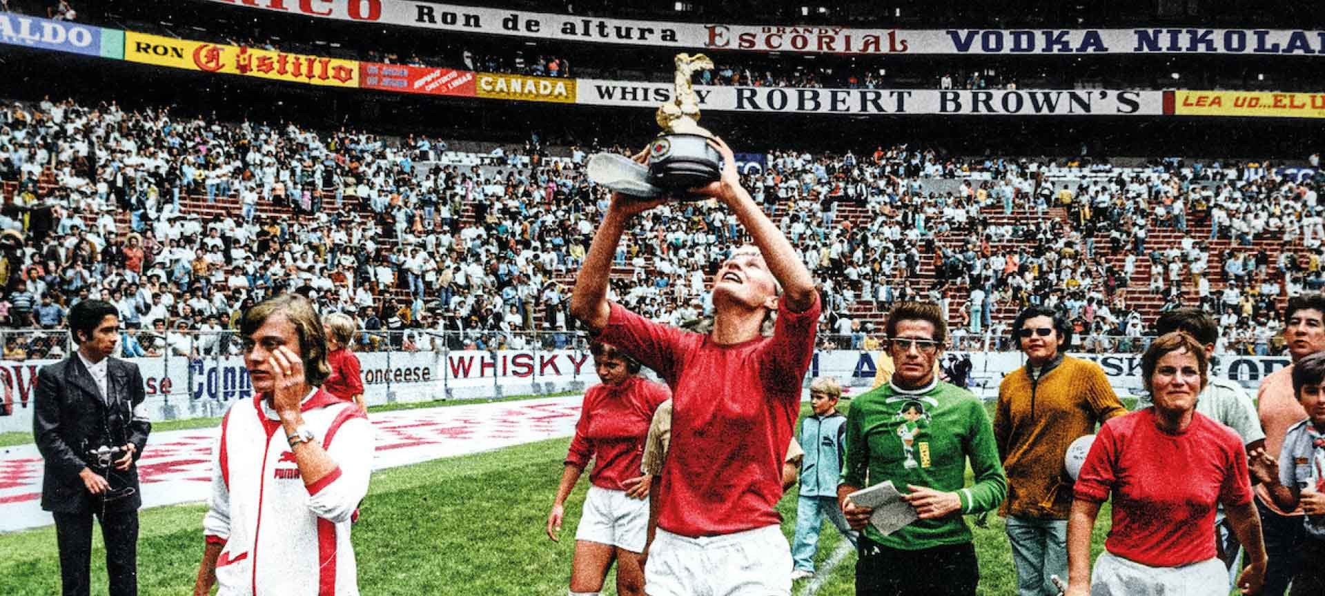 An image of a football team dressed in orange parading around a stadium as the central figure lifts the trophy at the 1971 Women's World Cup.