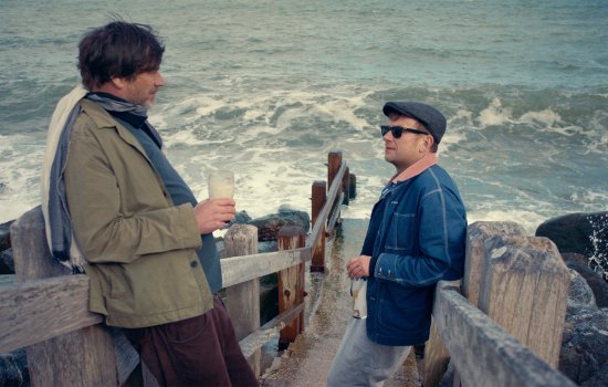 Two men stand side by side chatting next to the sea.