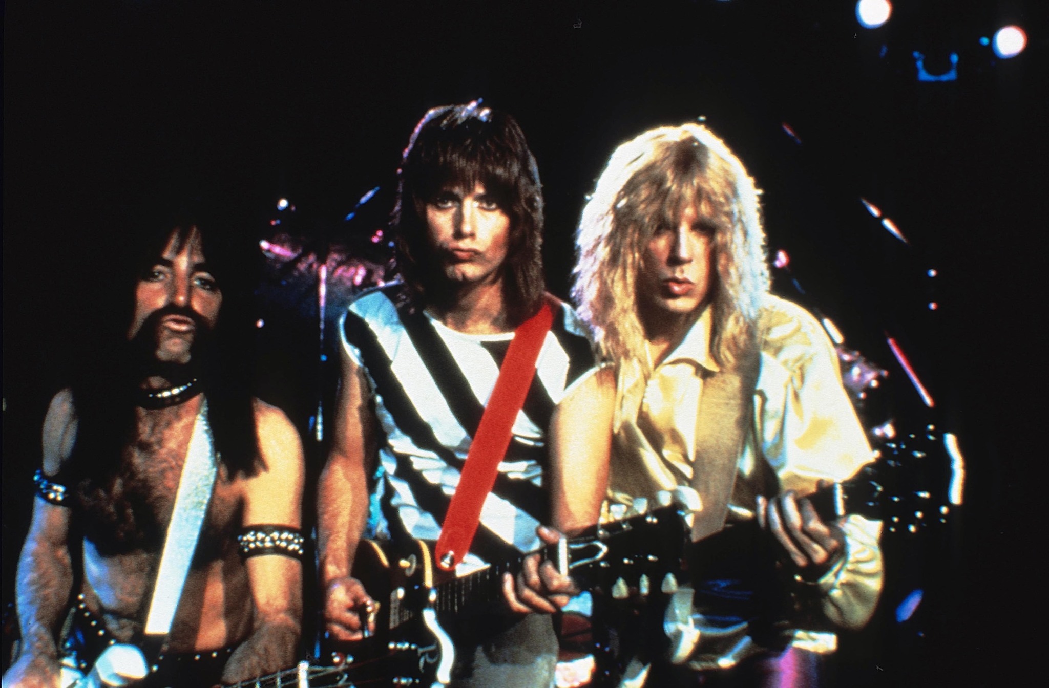 Three men stand side by side playing guitars on a stage.