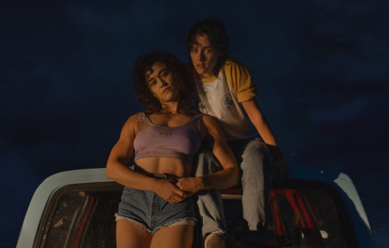 Two women sit on a car on a dark night.