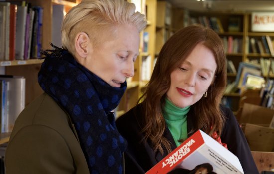 Tilda Swinton and Julianne Moore admire the back of a book in a bookshop.