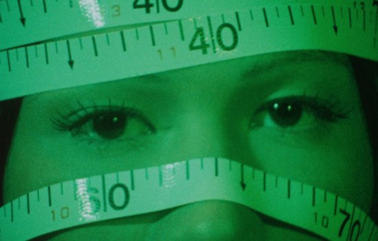 A woman's face is covered with measuring tape.