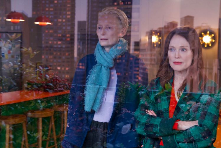 Tilda Swinton and Julianne Moore stand side by side looking out a window.