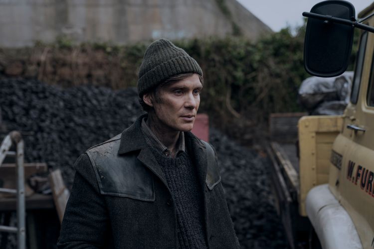 Cillian Murphy stands by a van on a grey day.