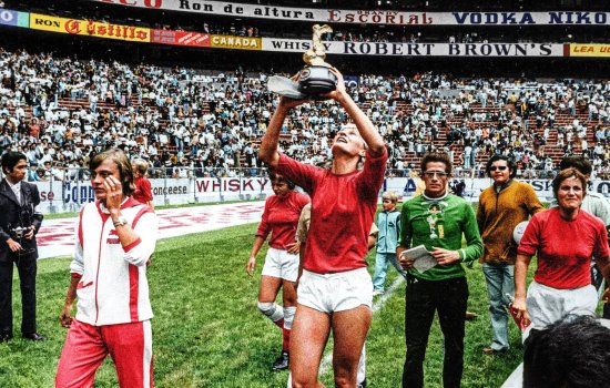 A group of football players in an orange kit parade around a stadium raising a trophy.