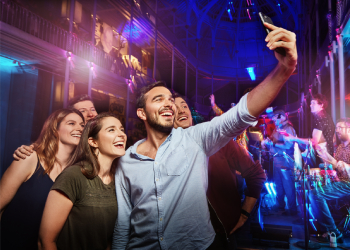 Five people in the Grand Gallery at night crowd round a man at the front with his arm outstretched taking a group selfie.