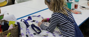 A child works on a white and lilac garment, surrounded by sewing supplies on a table.