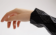 A hand and wrist point to the left. A structural, geometric black fabric is wrapped around the arm.