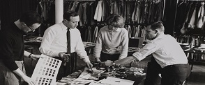 A black and white image of Bernat Klein and three colleagues (two men and one woman) are looking at cloth and yarn samples. 