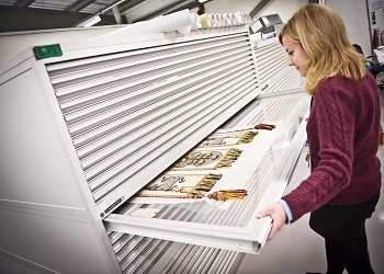 A woman is examining historic fabric in a drawer at the National Museum Collection Centre.