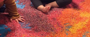Colourful rice is laid out on a floor ready to make art with. 