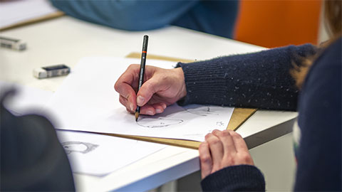 A detail of someone sketching using a pencil on paper.