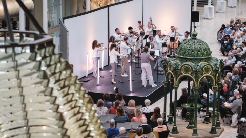 An orchestra is performing in the grand gallery at the National Museum of Scotland.