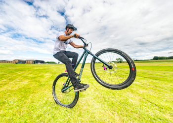 A stunt bike rider balances on their back wheel outdoors at the National Museum of Flight.