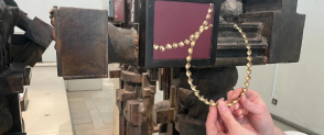 A pair of hands holding up a beaded loop in the Scotland galleries.