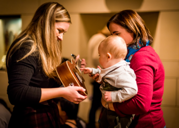 A visitor experience assistant shows a young visitor a guitar