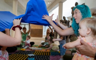 A number of young children sit with adults on a colourful carpet."