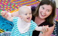 A baby smiles while a woman holds its hands. 