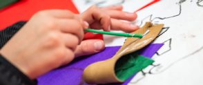 A pair of hands hold a paintbrush, adding glue to a piece of green felt. 