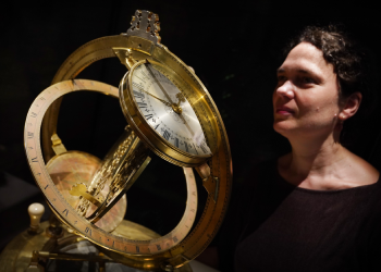 Dr Rebekah Higgitt stands next to a large golden dial, known as the Ilay Glynne dial, at the National Museum of Scotland