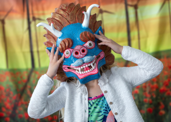 A child holds up a blue and pink dragon mask to their face. 