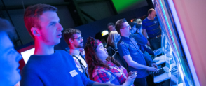 A long line of adults stand in front of gaming consoles at the Game On exhibition. 