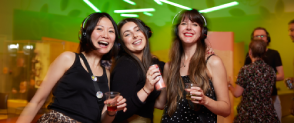 Three young women wear headsets while dancing in the Imagine Gallery. 