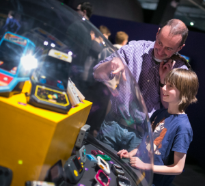 A woman stands in an exhibition space playing a retro game as part of the Game On exhibition.