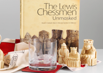 A selection of Lewis chess piece inspired gifts are display against a grey background. They include a book, whisky glass, physical chess pieces and a table cloth.