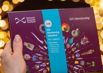 A gift membership pack is held aloft with a background of yellow blurred fairy lights.