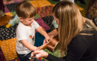 A young child plays with a ukulele held by a grown up woman.