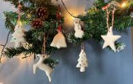Festive clay decorations of a Christmas tree, deer, bell and star hang from a Christmas tree branch.