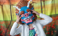 A young child hold up a dragon like multi-coloured mask.