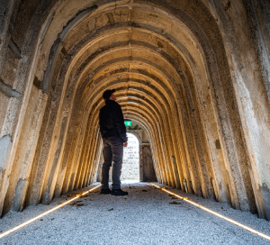 A man stands inside structure of concrete arches. 